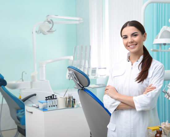 Young female dentist in white coat at workplace. Space for text