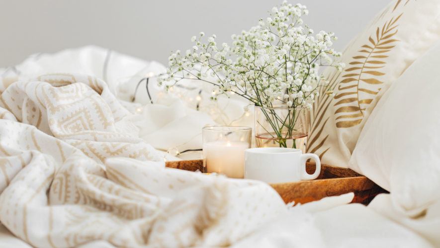 Wooden tray of coffee and candles with flowers on bed