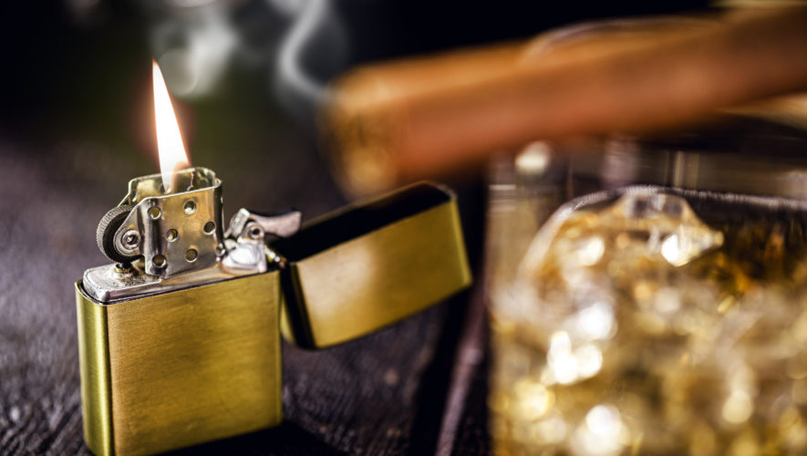 vintage windproof lighter on rustic wooden background. Access cigar and glass of alcohol in front, spot focus